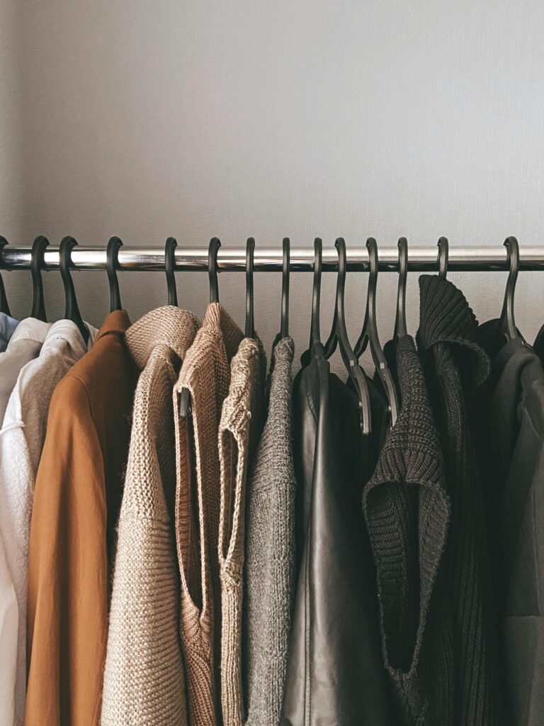 A collection of knitwear and sweaters hanging neatly on a closet rod.